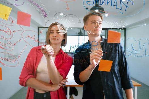 Couple of young creative start up business people brainstorming idea and solving problems by using sticky note and mind map at glass board, meeting room. discussing, working together. Immaculate.