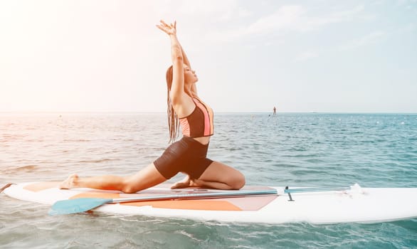 Woman sup yoga. Happy young sporty woman practising yoga pilates on paddle sup surfboard. Female stretching doing workout on sea water. Modern individual female outdoor summer sport activity