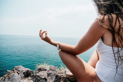 Woman meditating in yoga pose silhouette at the ocean, beach and rock mountains. Motivation and inspirational fit and exercising. Healthy lifestyle outdoors in nature, fitness concept.