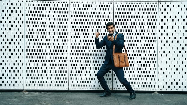 Happy skilled business man receive good news or getting a promotion while standing at white background. Smart executive manager happy and overjoy about successful project at city street. Exultant.