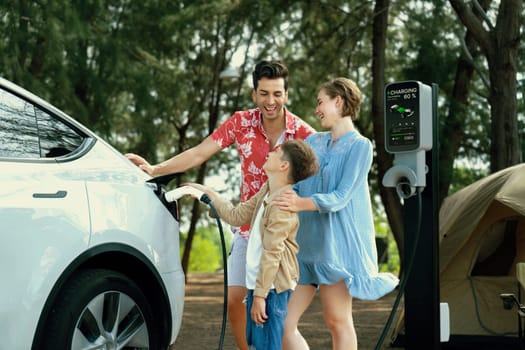 Outdoor adventure and family vacation camping in nature travel by eco friendly car for sustainable future. Lovely family recharge EV car with EV charging station in campsite. Perpetual