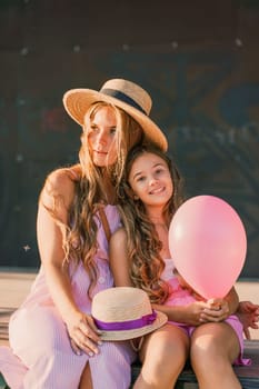 Portrait of mother and daughter in pink dresses with flowing long hair against the black backdrop. The woman hugs and presses the girl to her