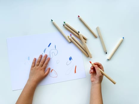 small child draws with colored pencils on paper on white table. High quality photo