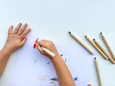 small child draws with colored pencils on paper on white table. High quality photo