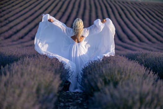 Blonde woman poses in lavender field at sunset. Happy woman in white dress holds lavender bouquet. Aromatherapy concept, lavender oil, photo session in lavender.