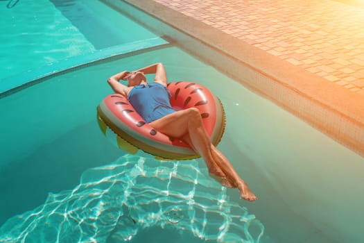 Happy woman in a swimsuit and sunglasses floating on an inflatable ring in the form of a watermelon, in the pool during summer holidays and vacations. Summer concept