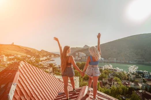 women standing on rooftop, enjoys town view and sea mountains. Peaceful rooftop relaxation. Below her, there is a town with several boats visible in the water. Rooftop vantage point