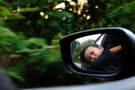 Focus on reflection of Asian kid on car rear view mirror.