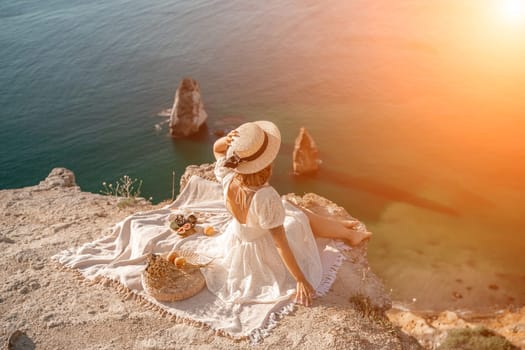 woman sea travel. photo of a beautiful woman with long blond hair in a pink shirt and denim shorts and a hat having a picnic on a hill overlooking the sea.