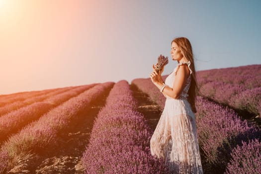 Close up portrait of young beautiful woman in a white dress and a hat is walking in the lavender field and smelling lavender bouquet.