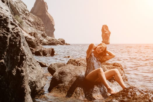 Woman travel sea. Young Happy woman in a long red dress posing on a beach near the sea on background of volcanic rocks, like in Iceland, sharing travel adventure journey