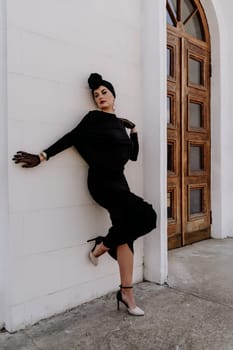 Stylish woman in the city. Fashion photo of a beautiful model in an elegant black dress posing against the backdrop of a building on a city street.