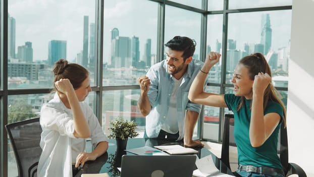 Professional business team receive a good news by using laptop while celebrate their success. Project manager high five and clap hands in front of laptop with colleague at modern office. Tracery