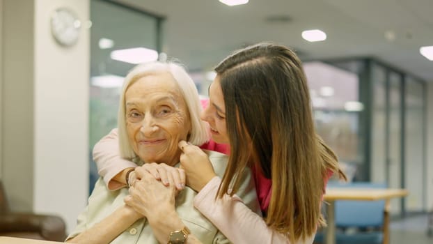 Photo of a smiling nurse that is a granddaughter embracing a senior woman in geriatrics
