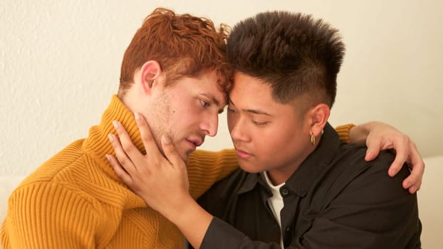 Multiethnic gay couple about to kiss sitting on the sofa