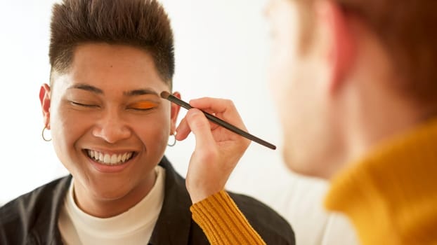 Gay man applying make up to her partner while smiling at home