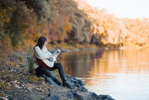 Beautiful autumn photo of a girl playing the guitar, enjoying bright colorful fall nature