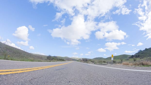 On a clear winter day, a car smoothly travels along Highway 101 near Santa Maria, California, under a brilliant blue sky, surrounded by a blend of greenery and golden hues.