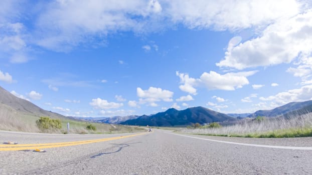 Vehicle is cruising along the Cuyama Highway under the bright sun. The surrounding landscape is illuminated by the radiant sunshine, creating a picturesque and inviting scene as the car travels through this captivating area.