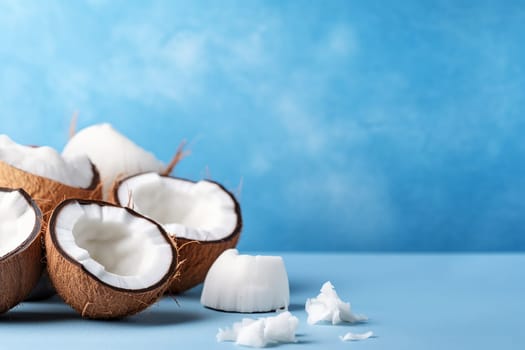 Halved coconuts on blue background with white coconut pieces