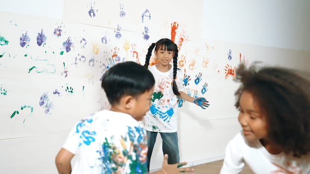 Playful children playing and running with colorful stained hand in front of white background. Funny happy multicultural students enjoy attending in art lesson. Creative activity concept. Erudition.