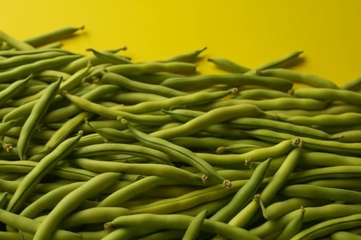 A pile of fresh green beans against a yellow background.