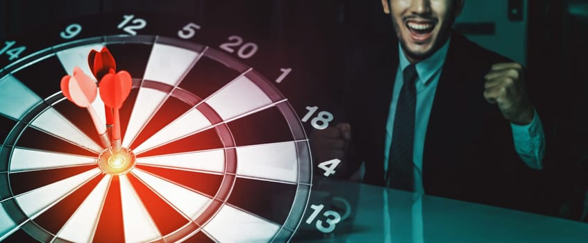 Business Target Goal For Success Strategy Concept - Red dart arrow hitting center goal on dart board with business people working in background showing precision and success of business target. uds