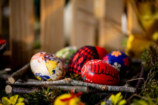 In this tranquil Easter scene, delicate handcrafted eggs rest in a basket lined with arranged twigs and lush green moss. One egg bears the inscription ,Alleluja, while the others feature floral patterns or colorful artistic doodles.