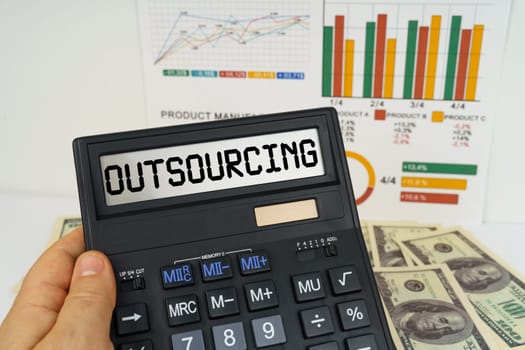 Business concept. On the table there are financial reports, dollars, in the hands of a calculator with the inscription - Outsourcing