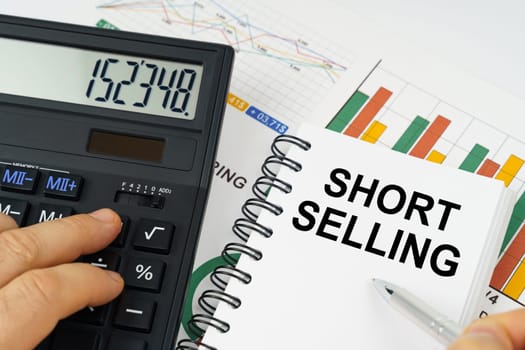 Business concept. On the table there is a calculator, reports with graphs and a notepad with the inscription - Short selling