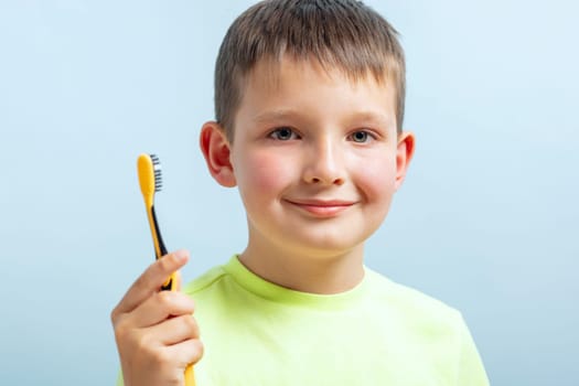 Portrait of a cheerful young boy holding a yellow toothbrush, promoting dental hygiene for children.