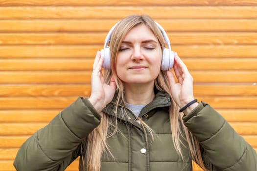 A content young woman with closed eyes enjoying music on white headphones against a wooden background.