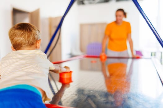 A boy enjoys an air hockey game with his mother at an indoor play center