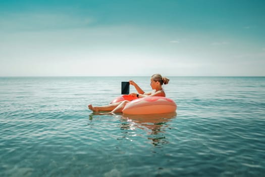 Woman laptop sea. Freelancer woman in sunglases floating on an inflatable big pink donut with a laptop in the sea. People summer vacation rest lifestyle concept