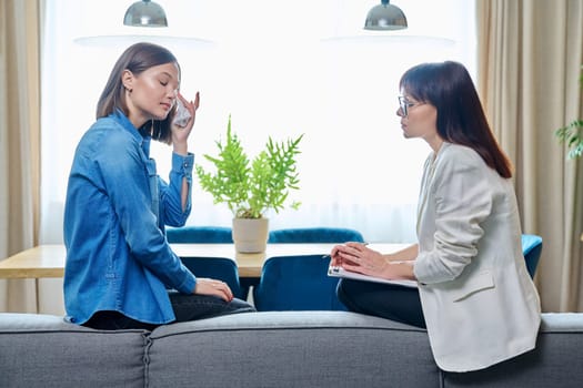 Sad crying young 20s woman in meeting with female psychologist therapist counselor sitting on couch in office. Psychology, therapy, psychotherapy, treatment, mental health, help, support