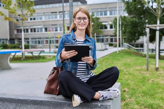 Girl student teenager outdoor near school building. Smiling teenage female with backpack digital tablet posing looking at camera. Adolescence, education, learning concept