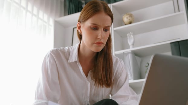 Young businesswoman sitting on the crouch using laptop computer for prim work on internet. Secretary or online content writing working at home. Remote working in domestic lifestyle/