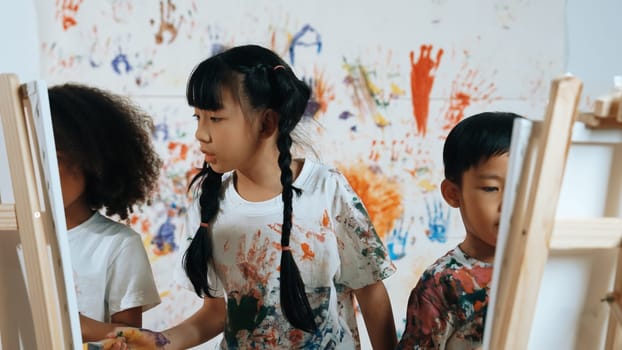 Playful student painted or draw canvas at stained wall with diverse friends in art lesson. Group of happy multicultural children working or create artwork at messy room. Creative activity. Erudition.