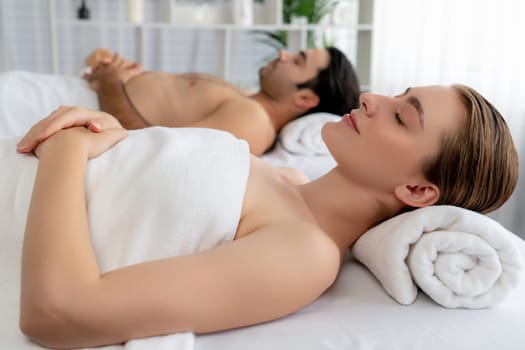 Caucasian couple customer enjoying relaxing anti-stress spa massage and pampering with beauty skin recreation leisure in day light ambient salon spa at luxury resort or hotel. Quiescent