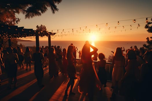 A crowd of people dancing and having fun at a beach party at sunset. Vacation concept.