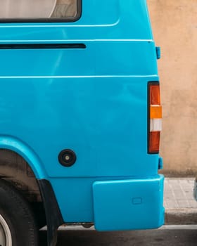 A close-up view of a bright blue vintage van's rear corner, highlighting its unique color and design