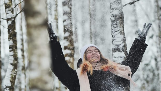 A girl is walking through the woods and kicking up snow in a birch forest