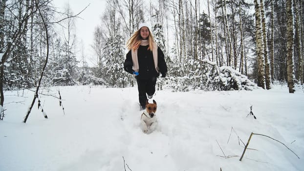 A girl and her Jack Russell Terrier dog are running through the woods