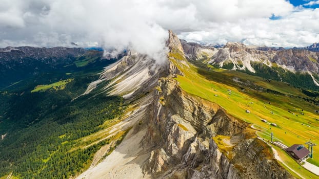 Seceda mountain with bare peak seen from tourist observation point. Giant ridgeline covered with green grass on slopes under cloudy sky aerial view