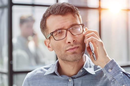 young man in a blue shirt talking on the phone in the office