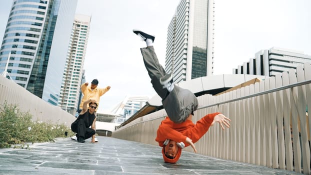 Young happy hipster perform break dancing or foot step with friend moving to hiphop music together. Skilled dancer doing freeze pose and waving hand. Modern lifestyle. Outdoor music 2024. Sprightly.