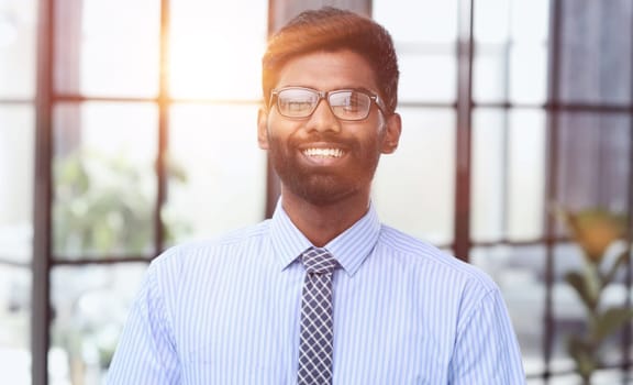 Confident elegant handsome young man standing in the office wearing a blue shirt