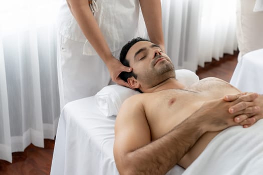 Caucasian man enjoying relaxing anti-stress head massage and pampering facial beauty skin recreation leisure in dayspa modern light ambient at luxury resort or hotel spa salon. Quiescent