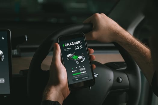 Electric car driver checks battery charging status, range and charging limit on app screen in the car. Smart technology device show EV car recharging data of electric storage in car battery innards.