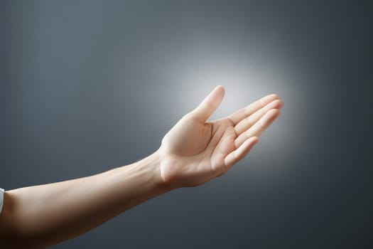 Light comes from a woman's hand against the background of a gray empty wall. Concept of spiritual life, support.
